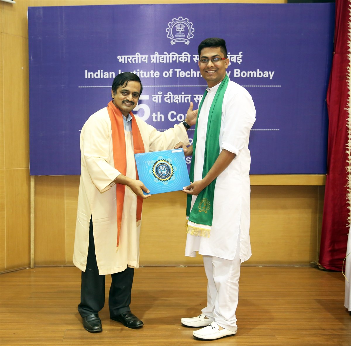 Amogh on stage in a white kurta and green stole, accepting a degree folder
                    from a faculty member in front of the Indian Institute of Technology Bombay
                    convocation backdrop.